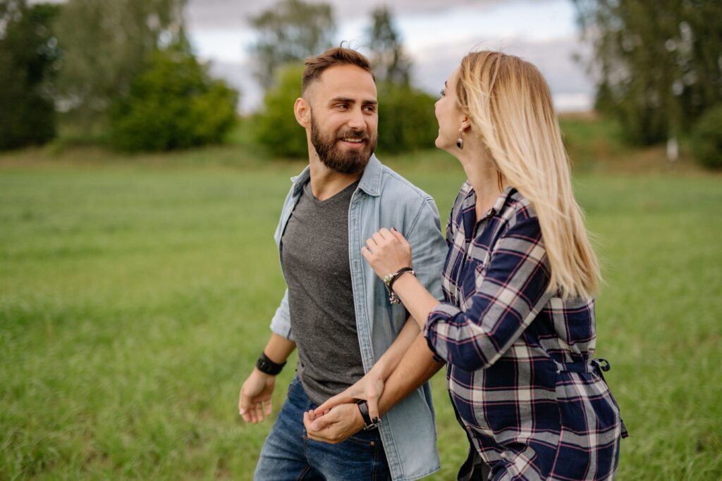 Smiling couple walking hand in hand across a green field, sharing a joyful moment.