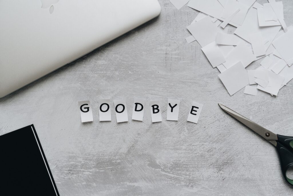 Artistic flat lay featuring the word 'GOODBYE' crafted from paper cutouts with scissors and a laptop.